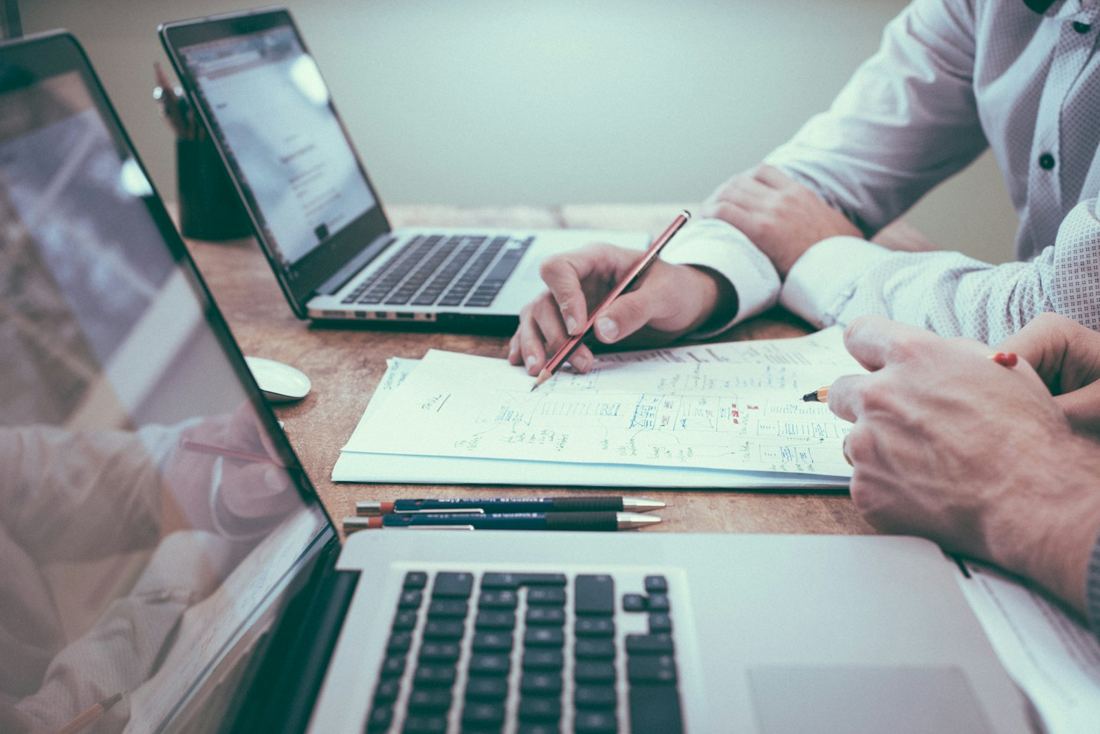 Manos revisando documentos de trabajo junto a una computadora portátil